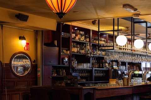 Het warme caféinterieur met donker houten lambrisering, lange bar en messing lampen.