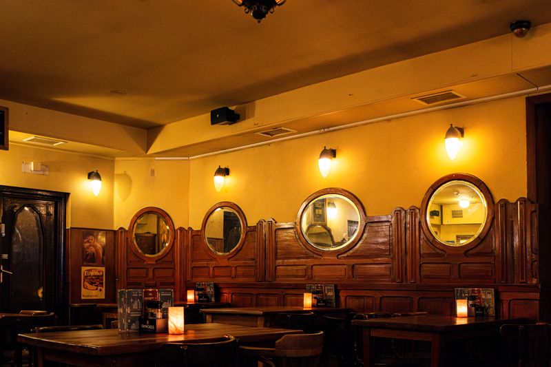 De achterzaal van het café bij avondlicht, met ronde spiegels aan de wand.