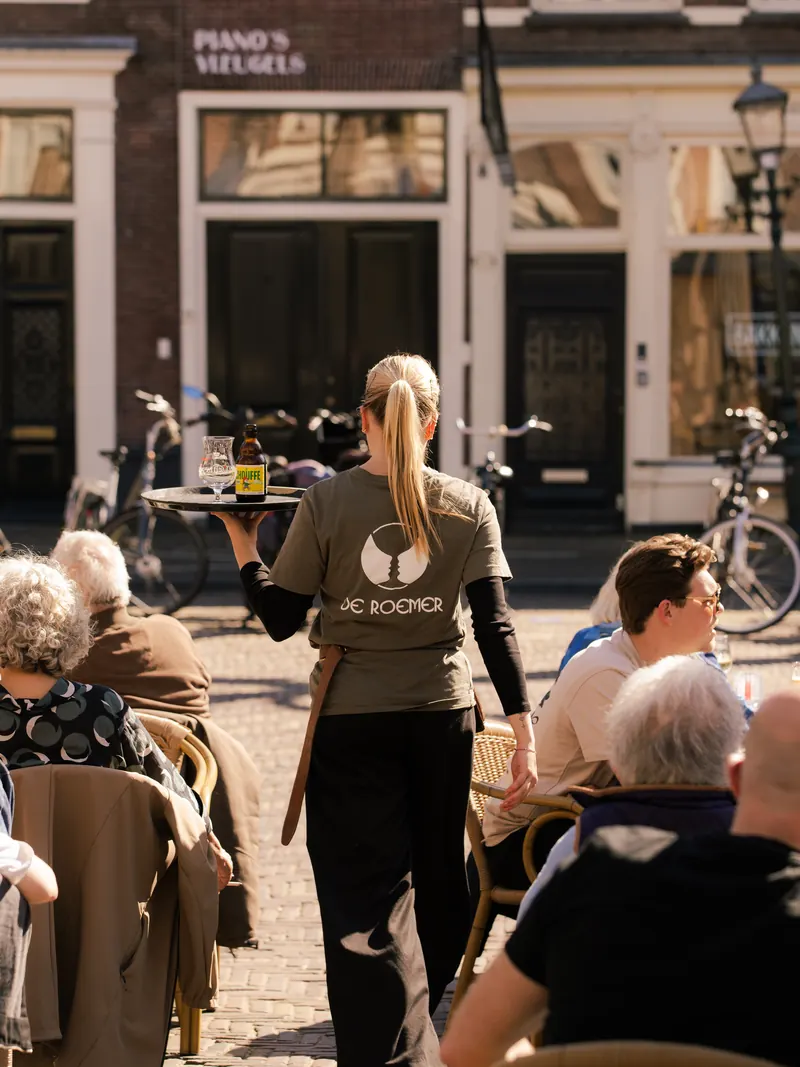 Een medewerker brengt drankjes naar gasten op het terras.