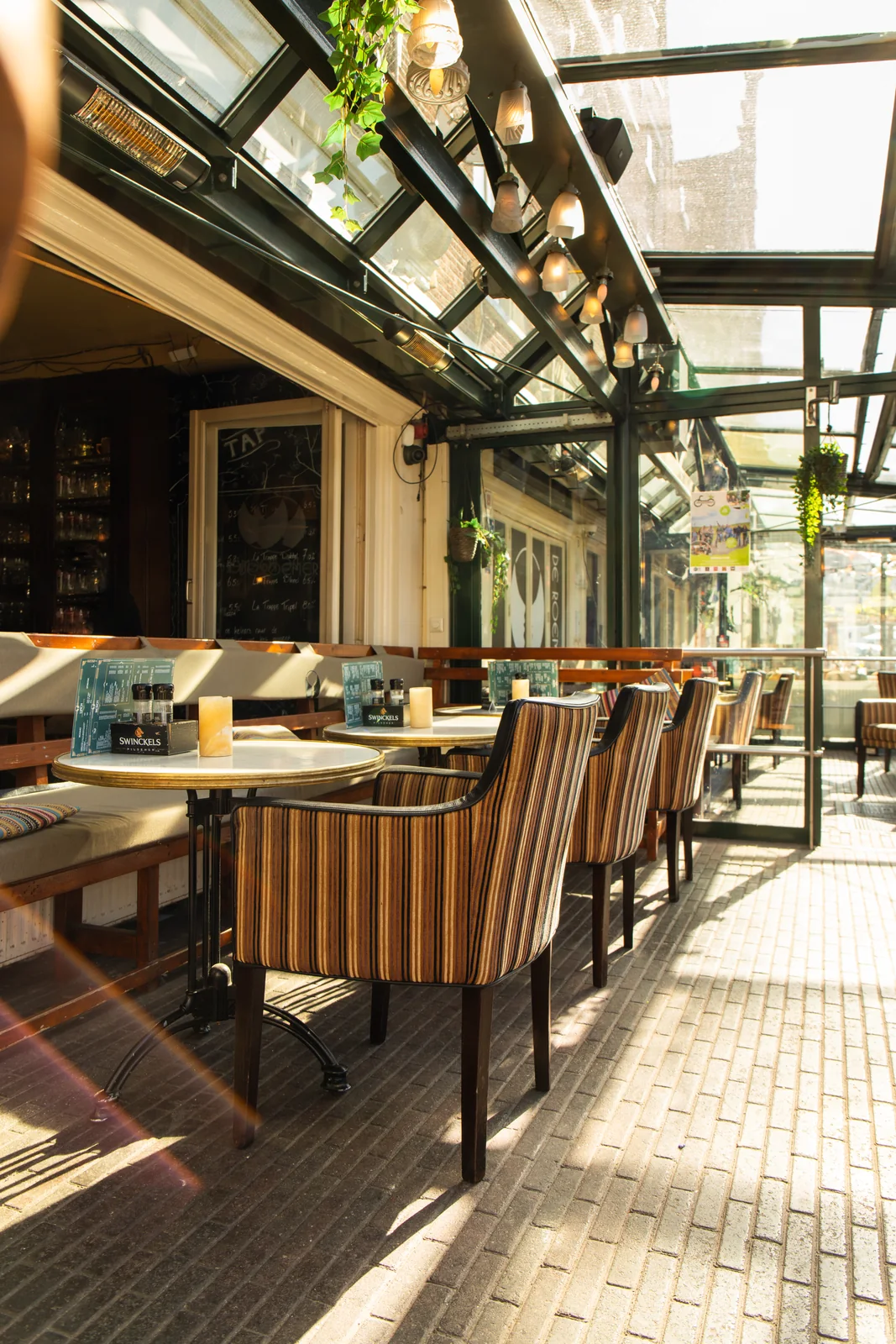 Lege glazen serre van Café de Roemer met gestreepte stoelen, ronde tafels en veel daglicht.